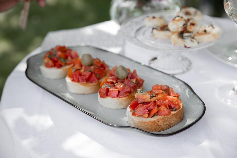 Ein Teller mit vier Bruschetta, belegt mit Tomaten und Oliven. Im Hintergrund sind weitere kleine Häppchen sichtbar. | © TV Südsteiermark - achromaticphotography