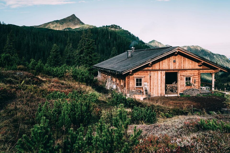 Eine gemütliche Hütte aus Holz in einer bergigen Landschaft. Im Hintergrund sind grüne Wälder und sanfte Hügel sichtbar. | © Armin Walcher