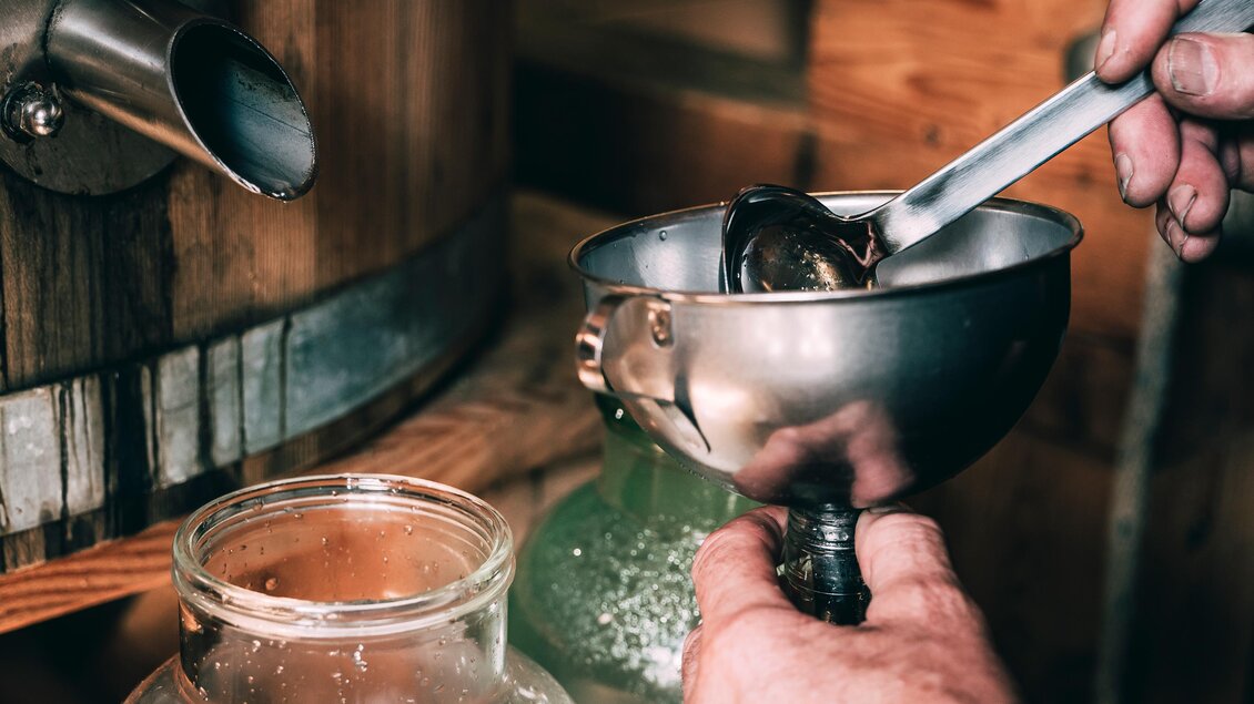 Eine Person verwendet einen Trichter, um eine Flüssigkeit in ein Glasgefäß zu füllen. Der Hintergrund zeigt Holz und weitere Utensilien. | © Armin Walcher