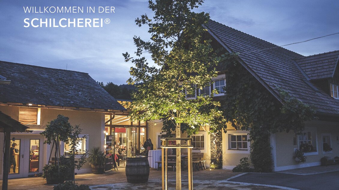 Ein einladendes Restaurant mit einem charmanten, hell erleuchteten Eingang. Zeitgemäße Architektur umgeben von grünem Baum und Garten. | © @Florian Jöbstl