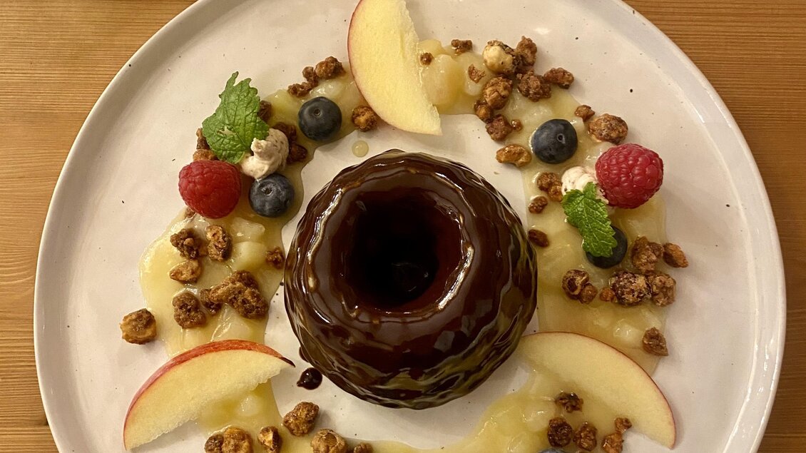 Ein köstlicher Dessertteller mit einem Schokoladenpflege und frischen Früchten. Umgeben von einer Garnitur aus Apfelstücken, Beeren und knusprigen Granola. | © Trieb