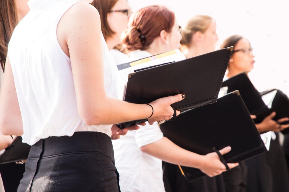 Eine Gruppe von Chormitgliedern in schwarz-weißer Kleidung. Sie halten Notenblätter in den Händen und singen zusammen. | © TV Südsteiermark_AdobeStock_73601166