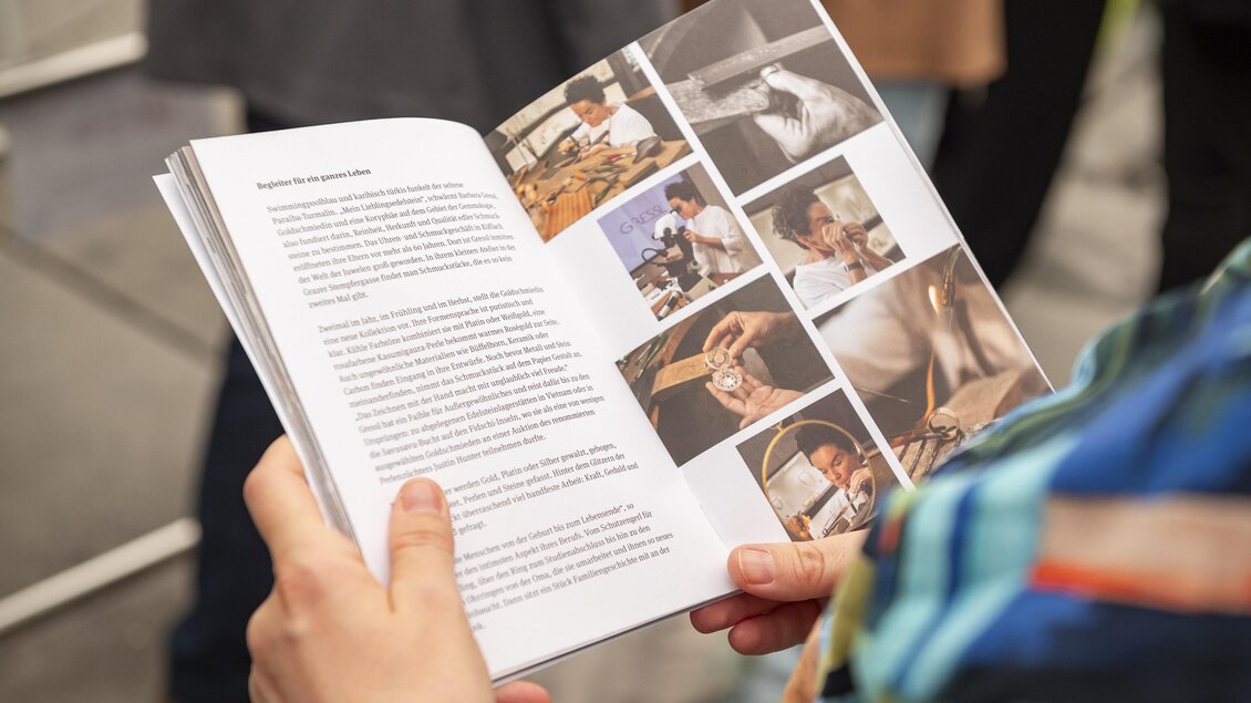 Eine Person hält einen geöffneten Ausstellungskatalog mit Texten und Fotos zum Handwerk auf der Murinsel in Graz. | © Bernd Grosseck