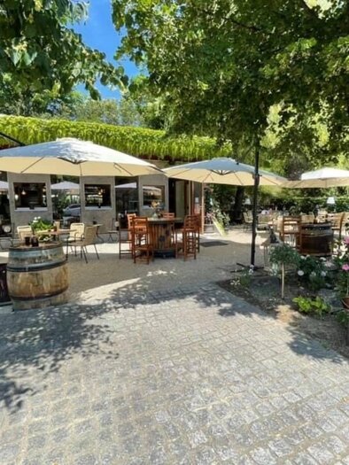 Ein einladendes Restaurant mit Außenbereich und Sonnenschirmen unter einem grünen Baum. Blumen und eine schöne Pflasterung runden die Atmosphäre ab. | © Weinkastl