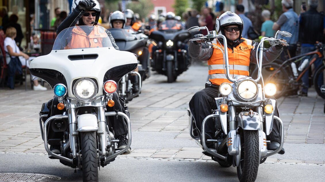 Zwei Motorräder fahren durch eine belebte Straße. Die Fahrer tragen Helme und orangefarbene Westen. | © Harald Steiner