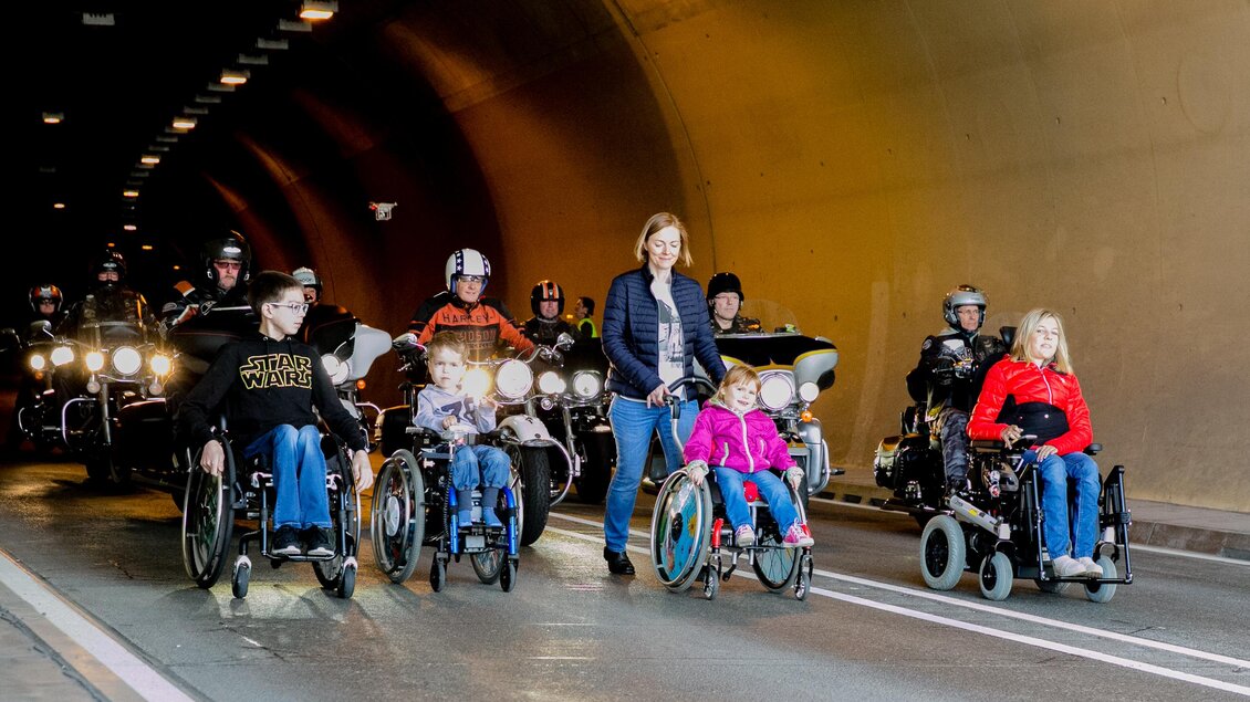 Eine Gruppe von Menschen in Rollstühlen geht durch einen Tunnel, begleitet von Motorradfahrern. Die Szene zeigt eine bewegende Verbindung zwischen den Teilnehmern und den Fahrern. | © Harley-Davidson Charity-Fonds