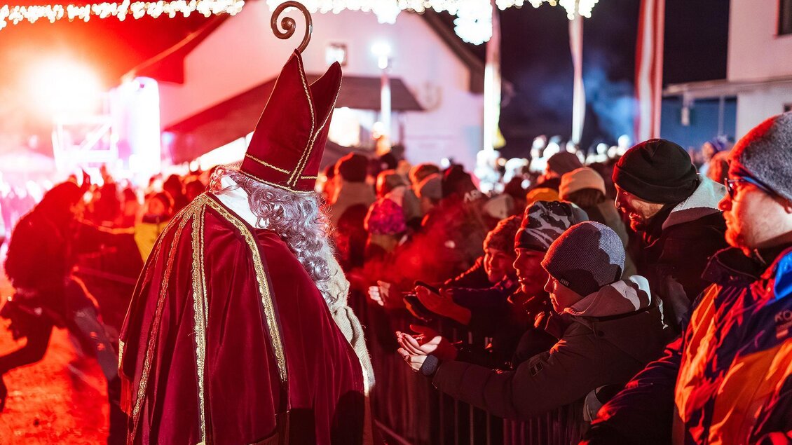 Eine festliche Szene mit einer Menschenmenge, die auf eine Person in einem roten Gewand schaut. Lichter dekorieren die Umgebung und schaffen eine weihnachtliche Atmosphäre. | © Fabian Anderle