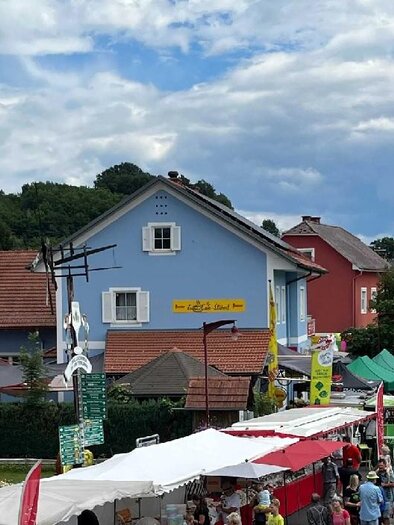 Bunter Heinrichsonntag in Unterlamm mit Marktständen, regionalen Produkten und Kirchturm im Hintergrund – lebendiges Dorffest. | © Gemeinde Unterlamm