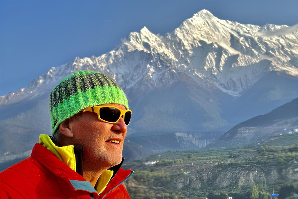 Ein Mann mit einer bunten Mütze und Sonnenbrille steht vor schneebedeckten Bergen. Der Himmel ist klar und die Landschaft wirkt majestätisch. | © Helmut Pichler