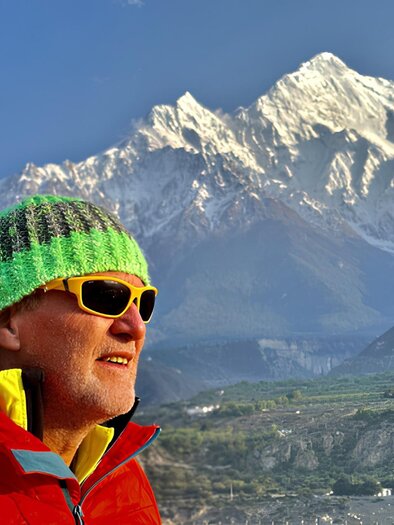 Ein Mann mit einer bunten Mütze und Sonnenbrille steht vor schneebedeckten Bergen. Der Himmel ist klar und die Landschaft wirkt majestätisch. | © Helmut Pichler