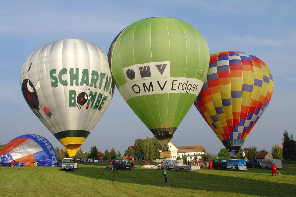 Eine malerische Weinlandschaft mit bunten Weinreben und einem klaren Himmel. Auf der rechten Seite genießen Menschen ein gemeinsames Essen im Freien. | © Ballonhotel Thaller
