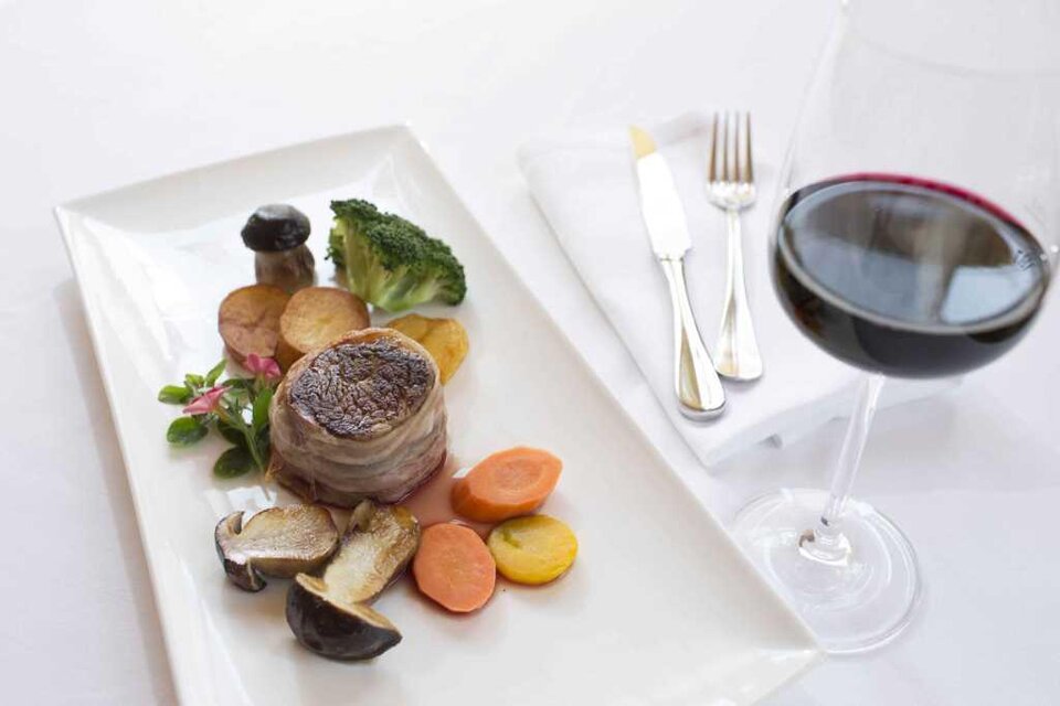 Ein köstliches Gericht mit saftigem Fleisch und buntem Gemüse. Dazu ein Glas Rotwein auf einem eleganten Tisch. | © Garten Hotel Ochensberger