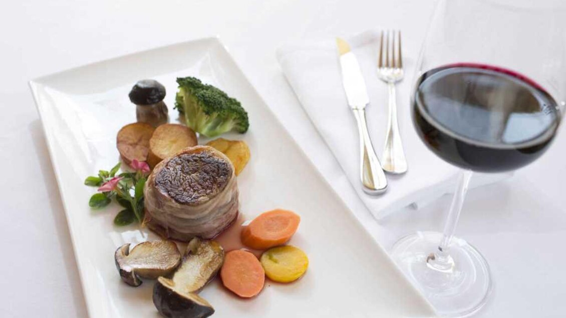 Ein köstliches Gericht mit saftigem Fleisch und buntem Gemüse. Dazu ein Glas Rotwein auf einem eleganten Tisch. | © Garten Hotel Ochensberger