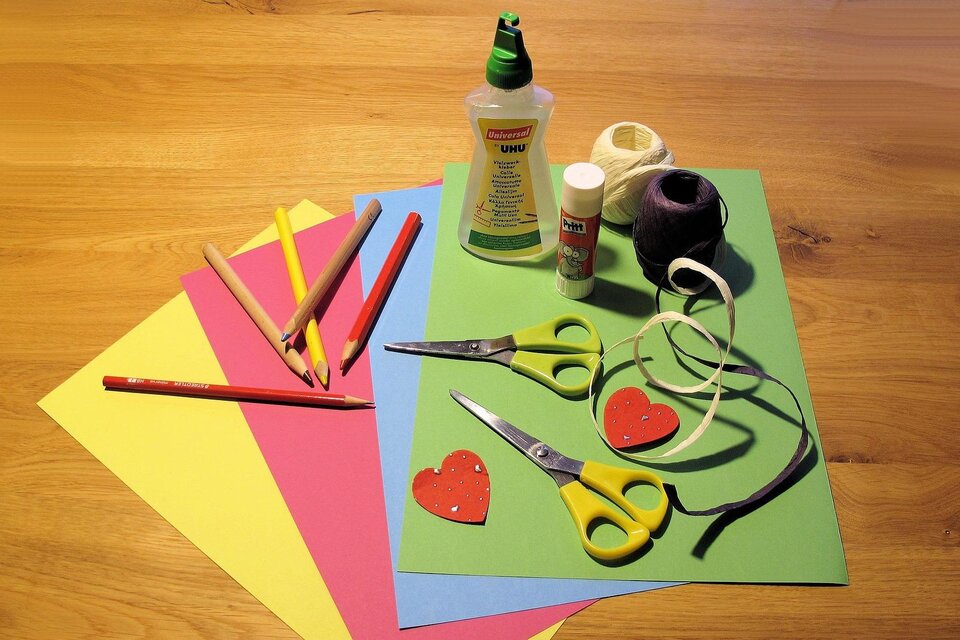 Eine Sammlung von Bastelmaterialien liegt auf einem Holztisch. Dazu gehören buntes Papier, Scheren, Kleber und Buntstifte. | © Pixabay