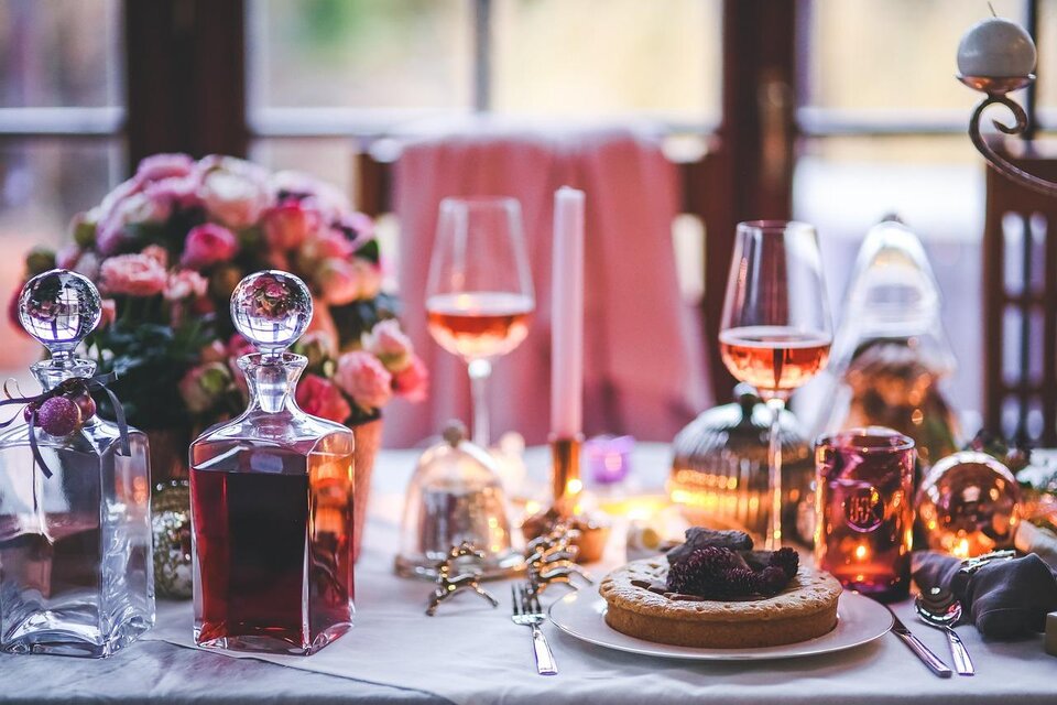 Ein festlich gedeckter Tisch mit feinen Gläsern und einer hübschen Blumendekoration. Auf dem Teller liegt ein köstlicher Kuchen, umgeben von warmem Licht. | © Pixabay.com