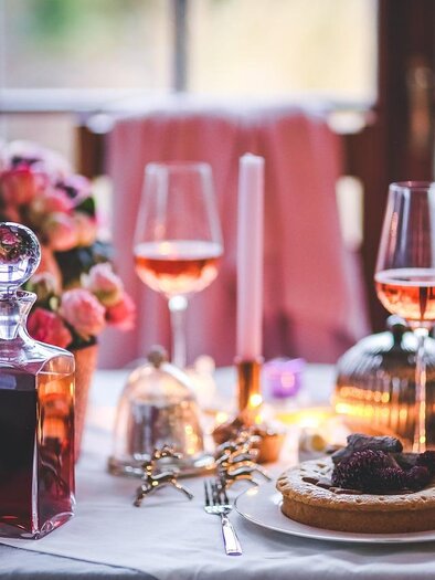Ein festlich gedeckter Tisch mit feinen Gläsern und einer hübschen Blumendekoration. Auf dem Teller liegt ein köstlicher Kuchen, umgeben von warmem Licht. | © Pixabay.com