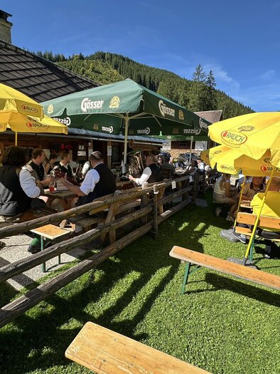 A cozy outdoor restaurant with several tables under sunny umbrellas. Guests enjoy their time in the beautiful nature. | © Thomas Rauninger