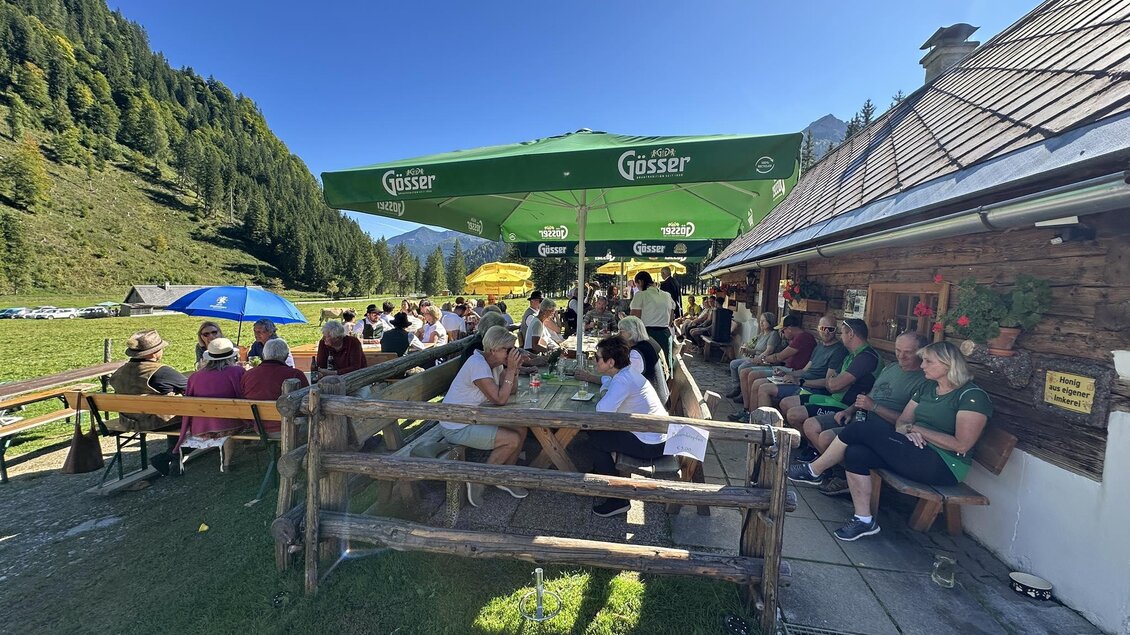 Ein gemütliches Café in den Bergen mit einer lebhaften Terrasse. Gäste genießen die Sonne unter großen Schirmen und umgeben von schöner Natur. | © Thomas Rauninger