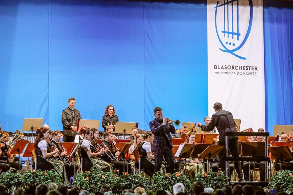 Ein Blasorchester spielt auf der Bühne. Der Dirigent leitet die Musiker, während das Publikum aufmerksam zuhört. | © Blasorchester voestalpine Donawitz