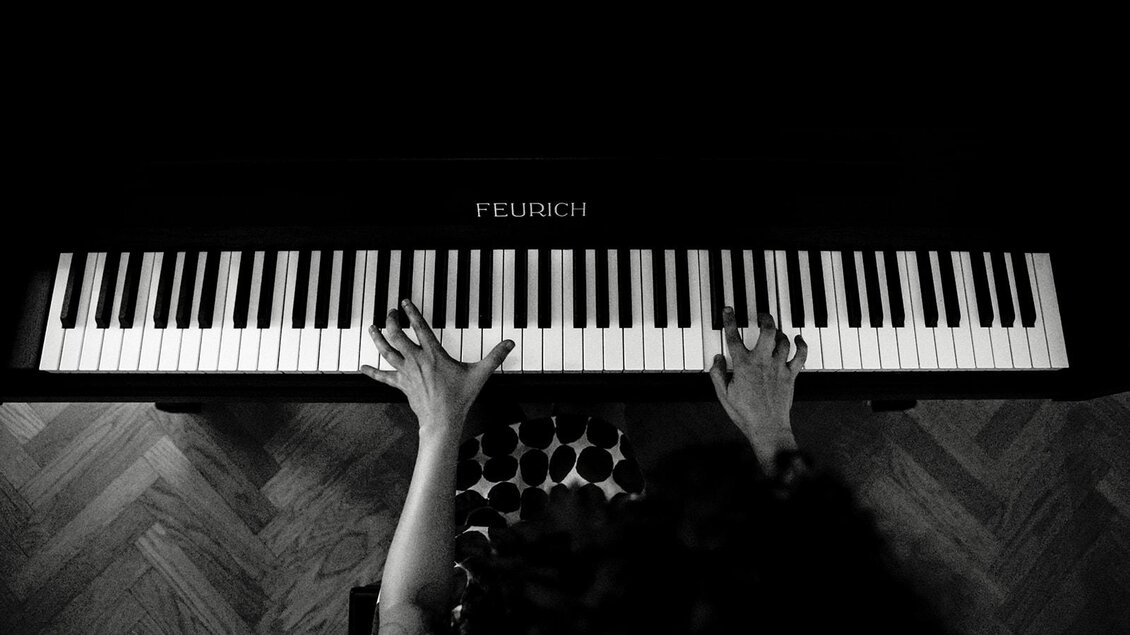 Eine Person spielt Klavier, ihre Hände sind über die Tasten platzieren. Der Hintergrund ist dunkel, was den Fokus auf das Klavier legt. | © TV Südsteiermark -achromaticphotography