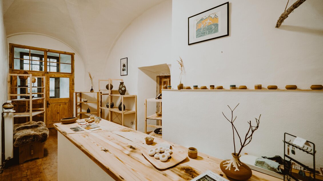 Ein heller Innenraum mit Holzregalen und handgemachten Keramiken. Auf einem langen Holztisch sind verschiedene Dekorationsobjekte und Kunstwerke ausgestellt. | © Karoline Karner