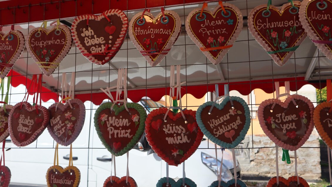 Eine Reihe von bunten Lebkuchenherzen hängt an einem Stand. Jedes Herz trägt eine verschiedene süße Botschaft oder einen Namen. | © Gemeinde Pölfing Brunn