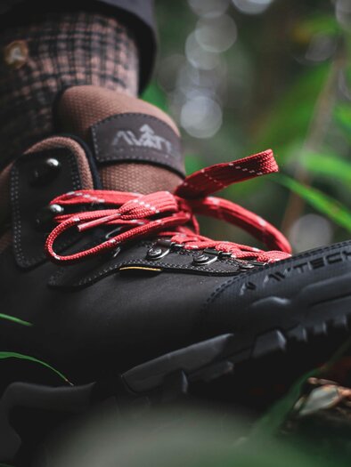 Ein Wanderschuh steht in dichter Vegetation. Die Schnürsenkel sind leuchtend rot und heben sich vom Schuh ab. | © baihaki-hine-unsplash