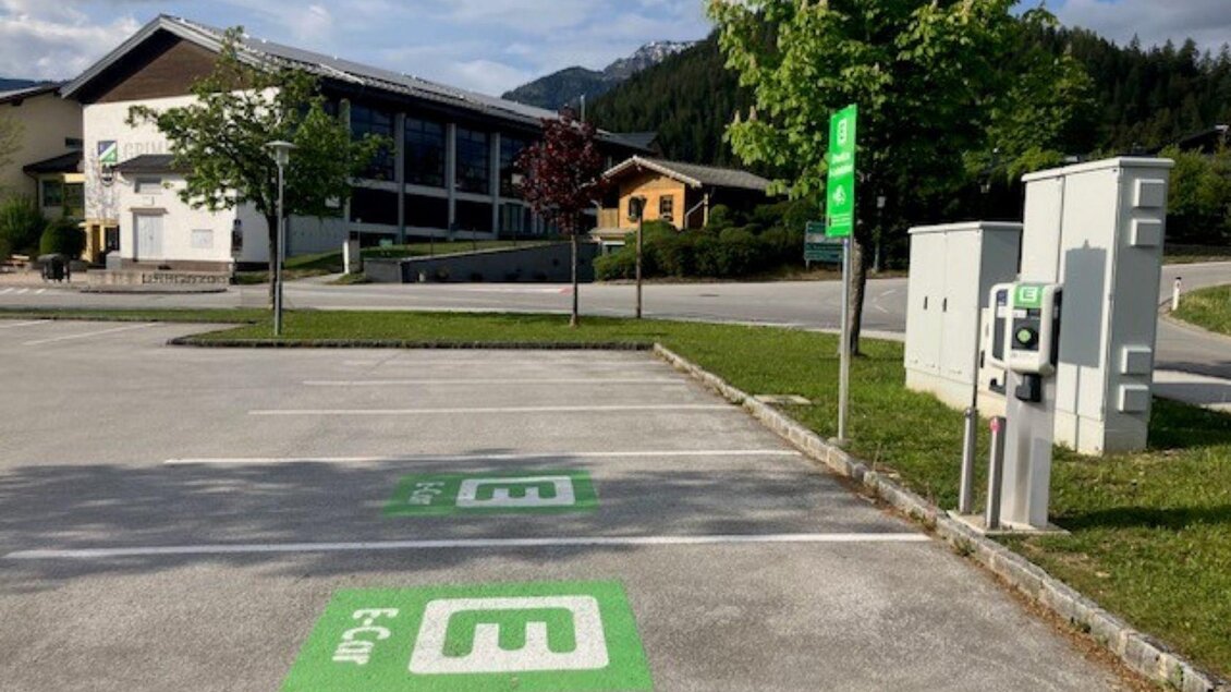Im Vordergrund ist der Parkplatz mit den E-Tankstellen und im Hintergrund ist die Grimminghalle, eine große Sporthalle im Zentrum von Bad Mitterndorf. | © Heike Temmel
