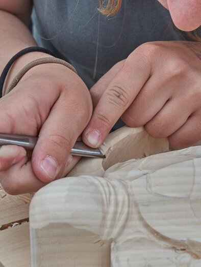 Eine Person schnitzt mit einem Werkzeug in ein Stück Holz. Die Hände sind konzentriert bei der Arbeit an der Holzfigur. | © RoyBuri | Pixabay.com