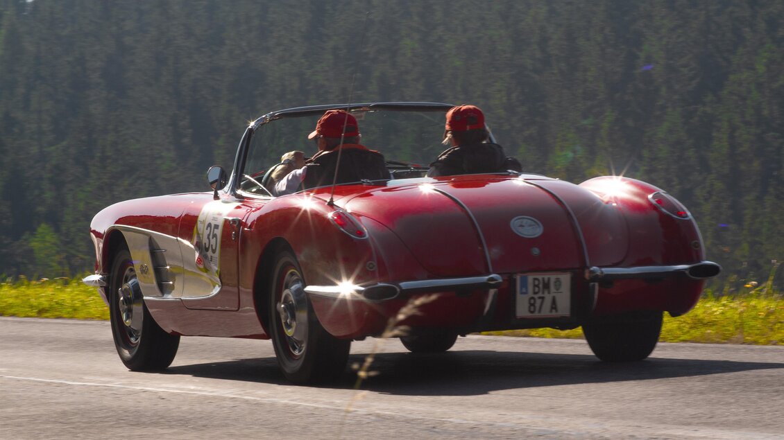 Ein rotes Sportcabriolet fährt auf einer kurvigen Straße. Im Hintergrund sind grüne Bäume und die Sonne scheint. | © HOSC Events OG