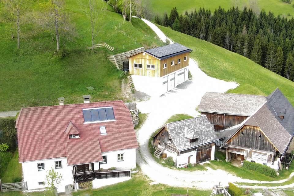 Eine ländliche Anlage mit mehreren Gebäuden auf einem Hügel. Die umgebende Landschaft ist grün und von Bäumen gesäumt. | © Fam. Gruber-Pfandl vlg. Totscher