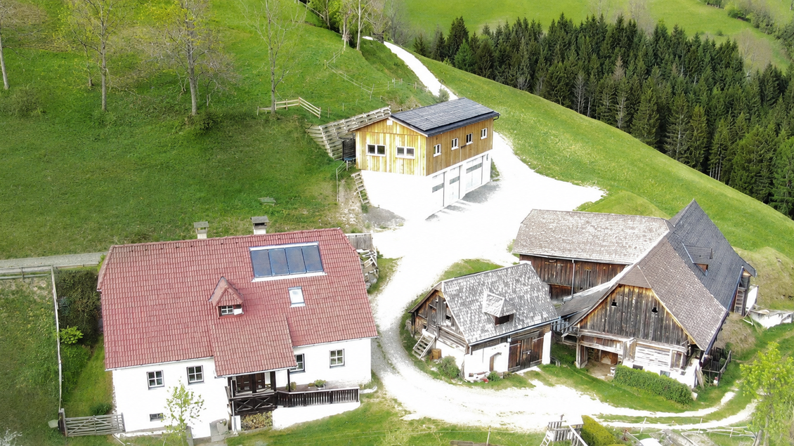 Eine ländliche Anlage mit mehreren Gebäuden auf einem Hügel. Die umgebende Landschaft ist grün und von Bäumen gesäumt. | © Fam. Gruber-Pfandl vlg. Totscher