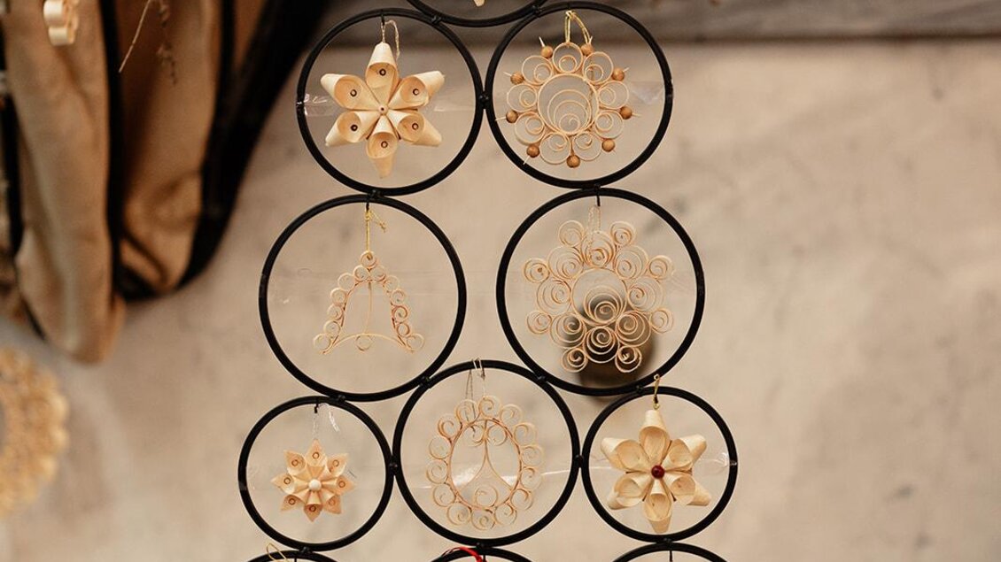 Ein dekorativer Weihnachtsbaum aus Metall, geschmückt mit kunstvollen goldenen Ornamenten. Im Hintergrund sind natürliche Elemente und eine festliche Tischdecke zu sehen. | © B Südsteiermark – Achromatic Photography