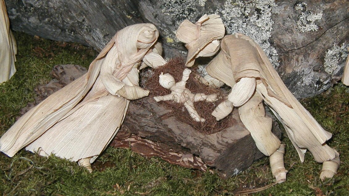 Eine Darstellung von Maria und Josef, die ein Kind in eine Wiege legen. Die Figuren sind aus natürlichen Materialien gefertigt und sind von einer rustikalen Umgebung umgeben. | © TV Südsteiermark