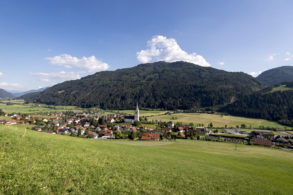 Eine malerische Berglandschaft mit einem kleinen Dorf und einer Kirche im Vordergrund. Der Himmel ist klar und die grünen Wiesen erstrecken sich bis zum Horizont. | © TV Murau