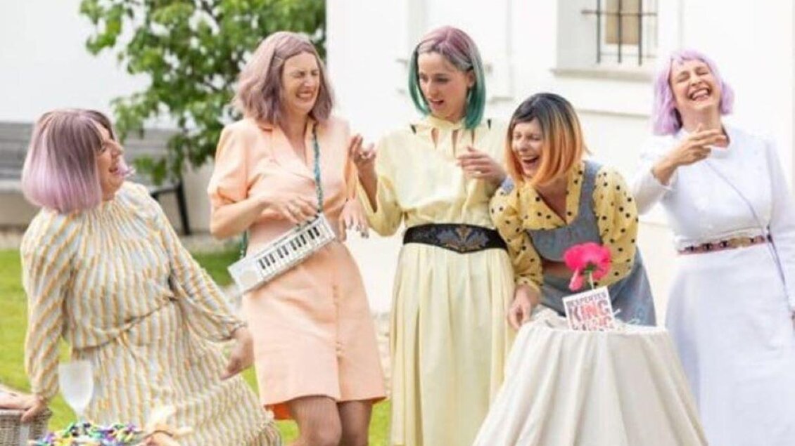 Eine Gruppe von fünf Frauen mit bunten Haaren feiert fröhlich im Freien. Sie tragen modische Outfits und lachen miteinander. | © Nikola Milatovic