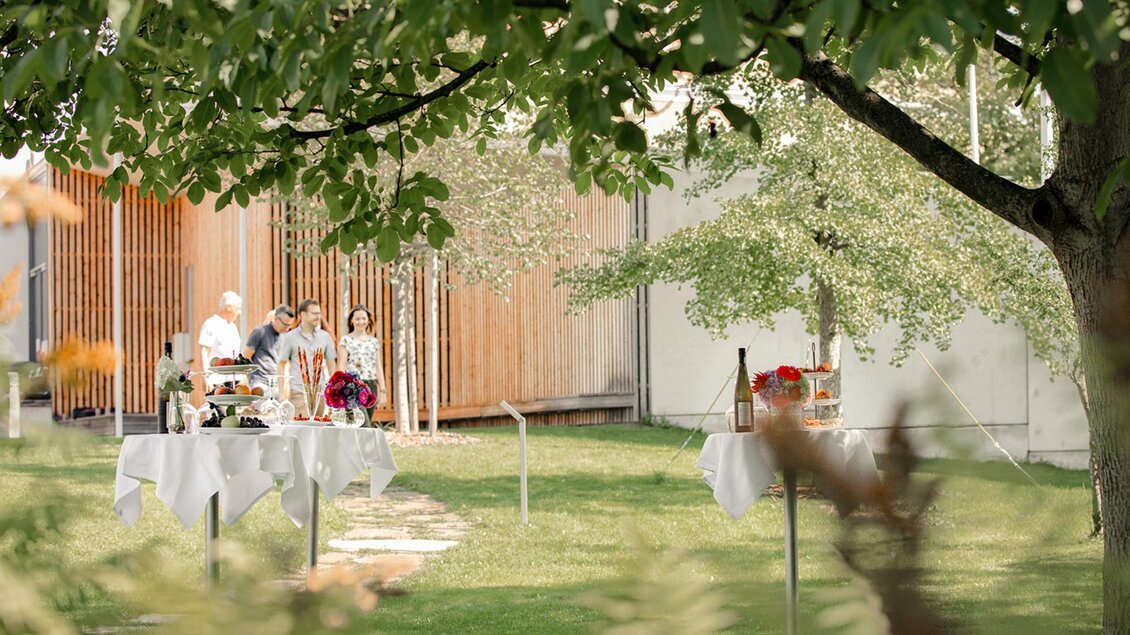 Ein schöner Garten mit gedeckten Tischen und einer entspannenden Atmosphäre. Im Hintergrund sind Personen in lebhaftem Austausch zu sehen. | © Stieglerhaus - achromaticphotography