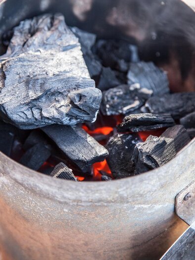 Ein Grillanzünder mit glühenden Holzkohlebriketts. Der Rauch steigt nach oben und zeigt, dass die Kohlen bereit zum Grillen sind. | © Pixabay