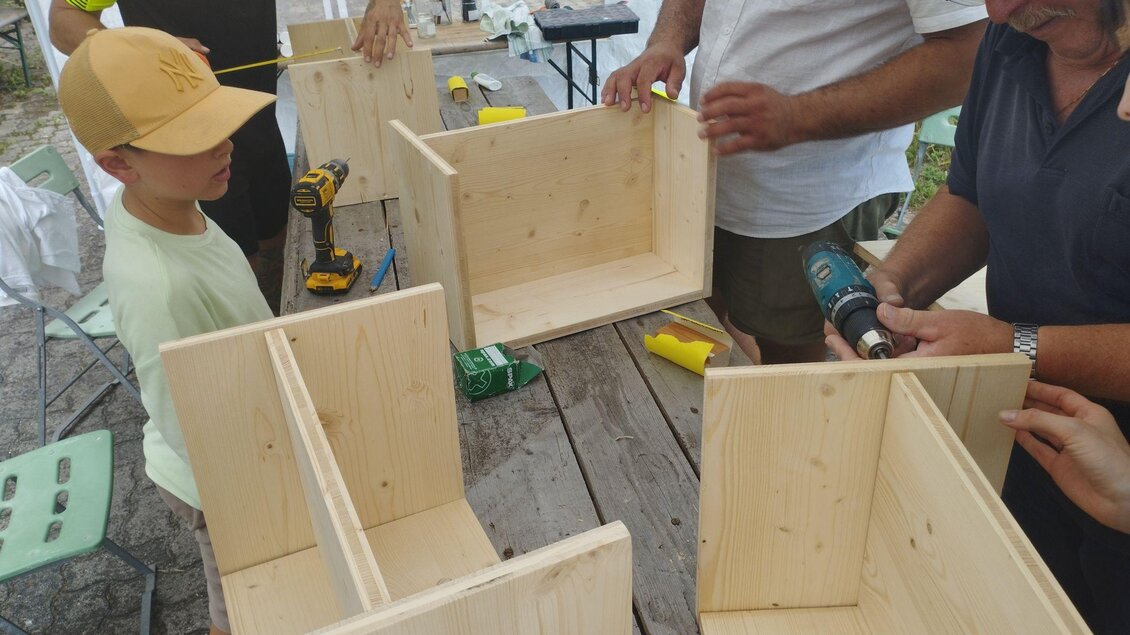 Eine Gruppe von Personen baut Holzkästen zusammen. Werkzeuge und Materialien liegen auf einem Tisch im Freien. | © Johanna Schriebl