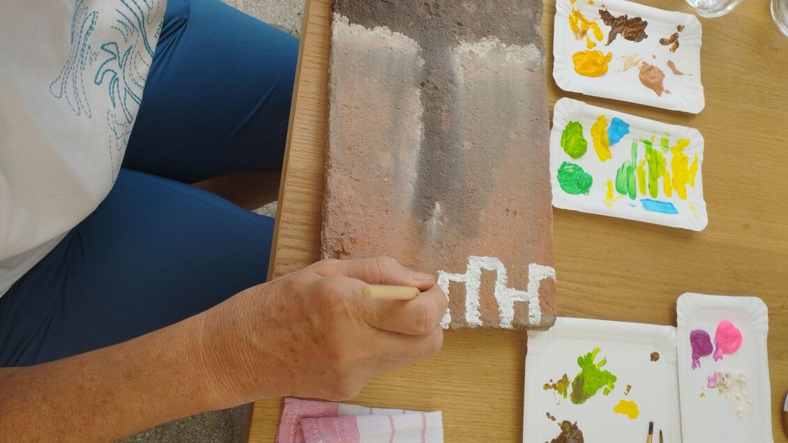 Eine Person malt auf einer Steinplatte mit verschiedenen Farben. Neben ihr befinden sich Paletten mit weiteren Farben und Pinsel. | © Johanna Schriebl