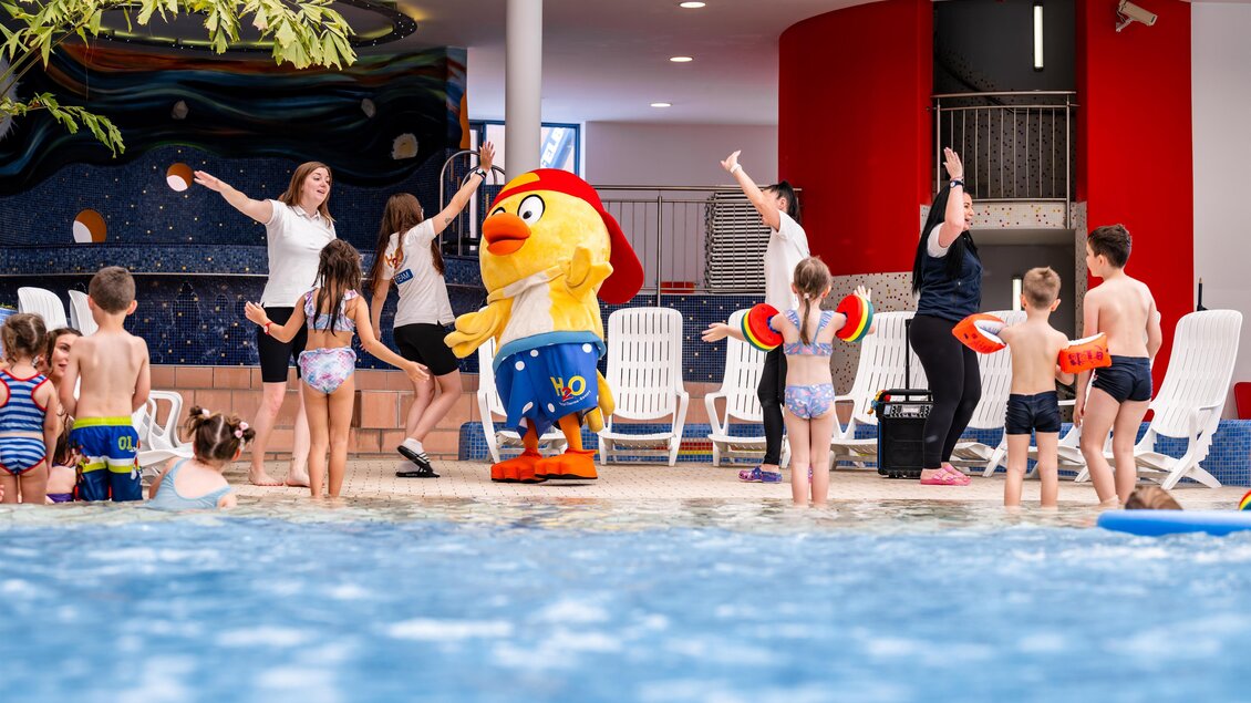Eine fröhliche Poolparty mit Kindern und einem Maskottchen. Die Kinder genießen das Wasser und tanzen. | © H2O-Hoteltherme GmbH / moving Stills