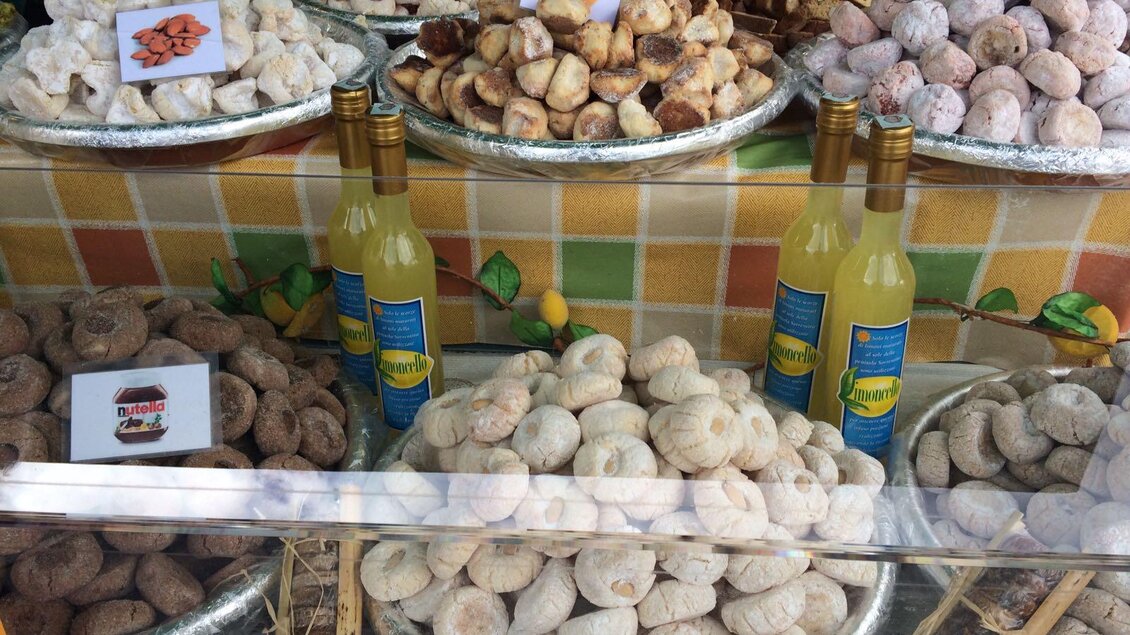Eine Auswahl an süßen italienischen Spezialitäten in verschiedenen Formen und Geschmacksrichtungen ist in einer Vitrine angeordnet. Neben den Süßigkeiten stehen vier Flaschen Limoncello. | © TVB Ausseerland Salzkammergut