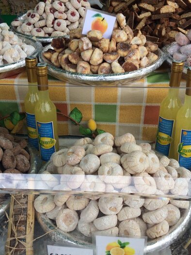 A selection of sweet Italian specialties in various shapes and flavors is arranged in a display case. Next to the sweets are four bottles of limoncello. | © TVB Ausseerland Salzkammergut