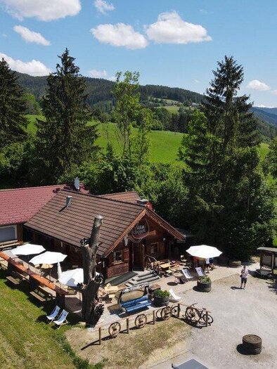 Eine idyllische Berghütte umgeben von grüner Wiese und Bäumen. Auf der Terrasse stehen Tische und Stühle unter Sonnenschirmen. | © Marcus Auer