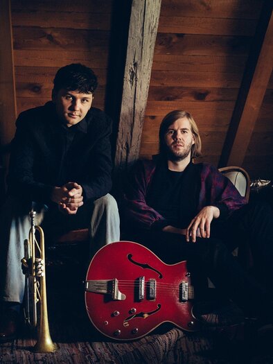 Zwei Musiker sitzen in einem rustikalen Raum. Einer hält eine Trompete und der andere eine rote Gitarre. | © jazzfestival