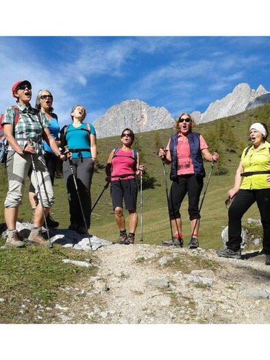 Eine Gruppe von Wanderern steht auf einem Weg in den Bergen. Die Sonne scheint und die Landschaft ist grün und hügelig. | © Härtel Ingeborg