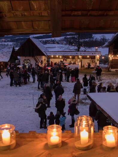 Ein festlicher Weihnachtsmarkt bei Nacht, beleuchtet von Kerzen und Lichtern. Menschen schlendern zwischen den Ständen und genießen die gemütliche Atmosphäre. | © Klaudia Riebenbauer