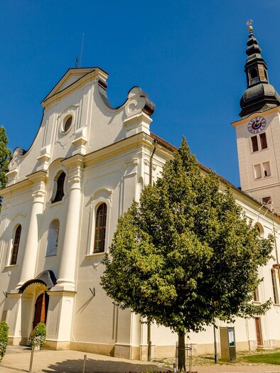 Eine schöne Kirche mit einer hohen Turmuhr und einem klaren Himmel. Umgeben von Bäumen und einer gepflegten Landschaft. | © @Wolfgang Spekner