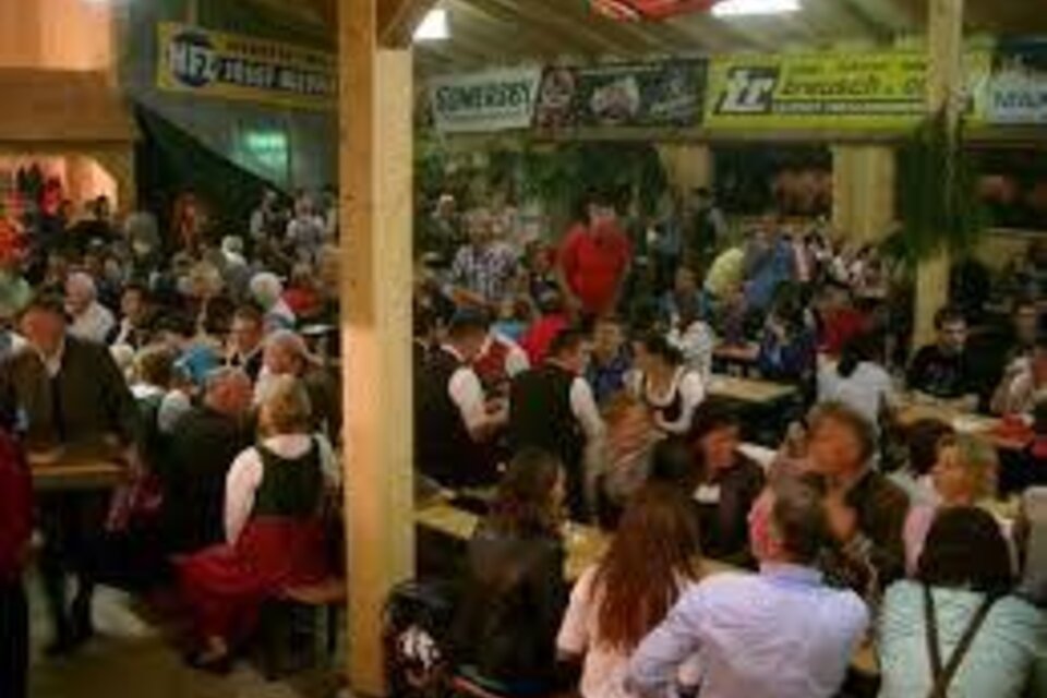 Ein lebhaftes Festival mit vielen Menschen, die an langen Tischen sitzen und feiern. Die Gäste tragen traditionelle Kleidung und die Atmosphäre ist festlich.