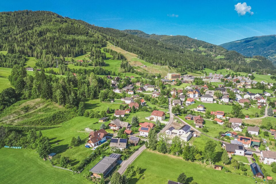 Eine malerische Landschaft mit grünen Hügeln und einem kleinen Dorf. Die Häuser sind umgeben von Wäldern und Wiesen.